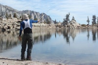 a man is fishing near a lake with mountains in the background